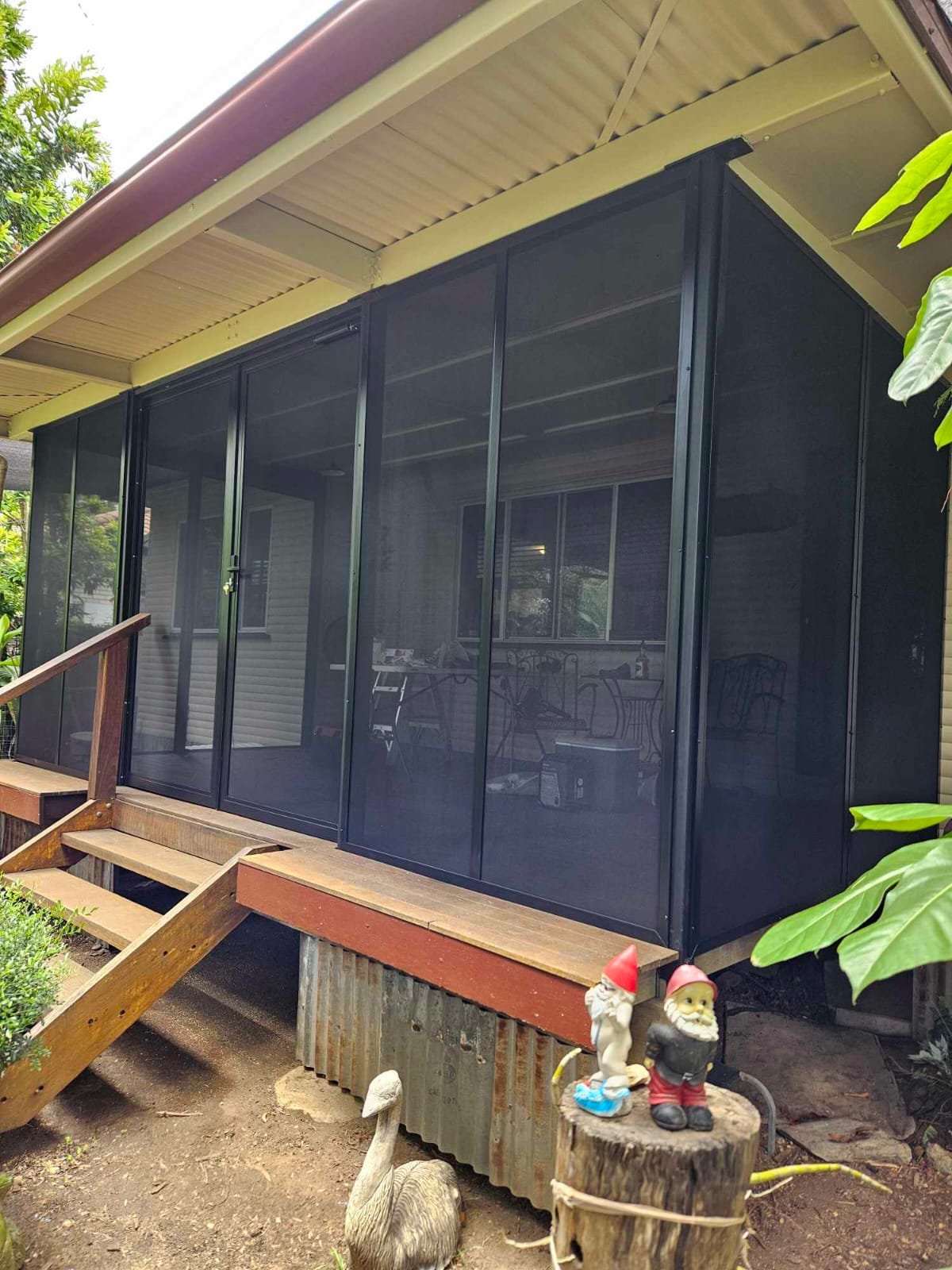 Timber deck patio fully enclosed in black framed security mesh, with a tropical garden beyond