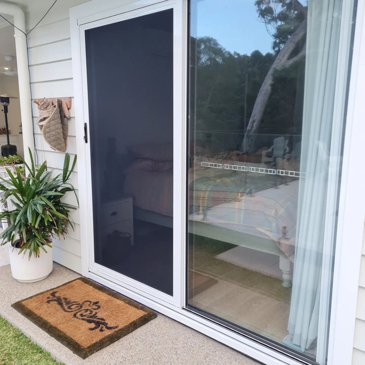 White framed sliding security door at a front entry with a pot plant and doormat