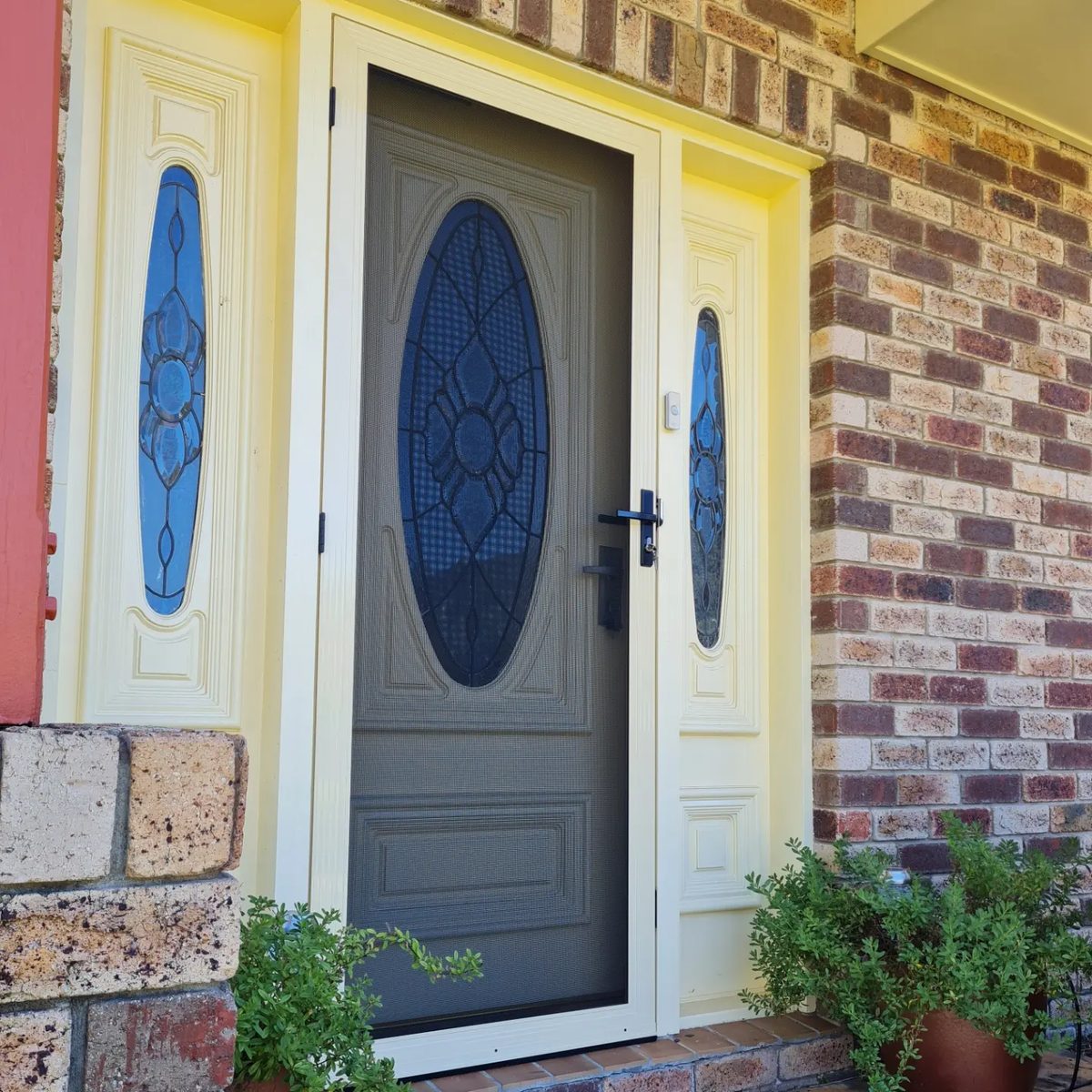 Cream hinged security door over a leadlight front door on a brick home