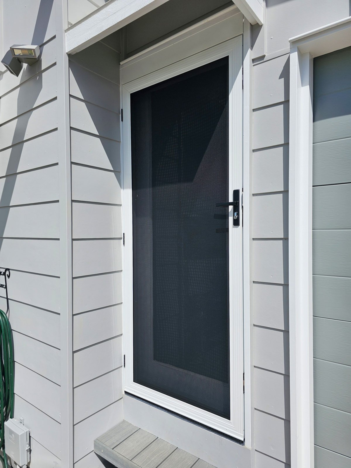 White framed SecureView hinged security door on a grey weatherboard home entry